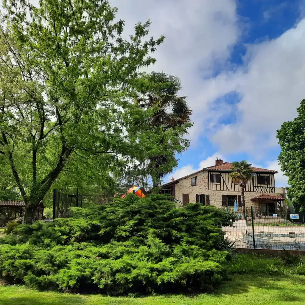 Vue de la maison en pierre du Domaine du Castex, entourée de verdure et de grands arbres, typique d’un camping à Aignan.